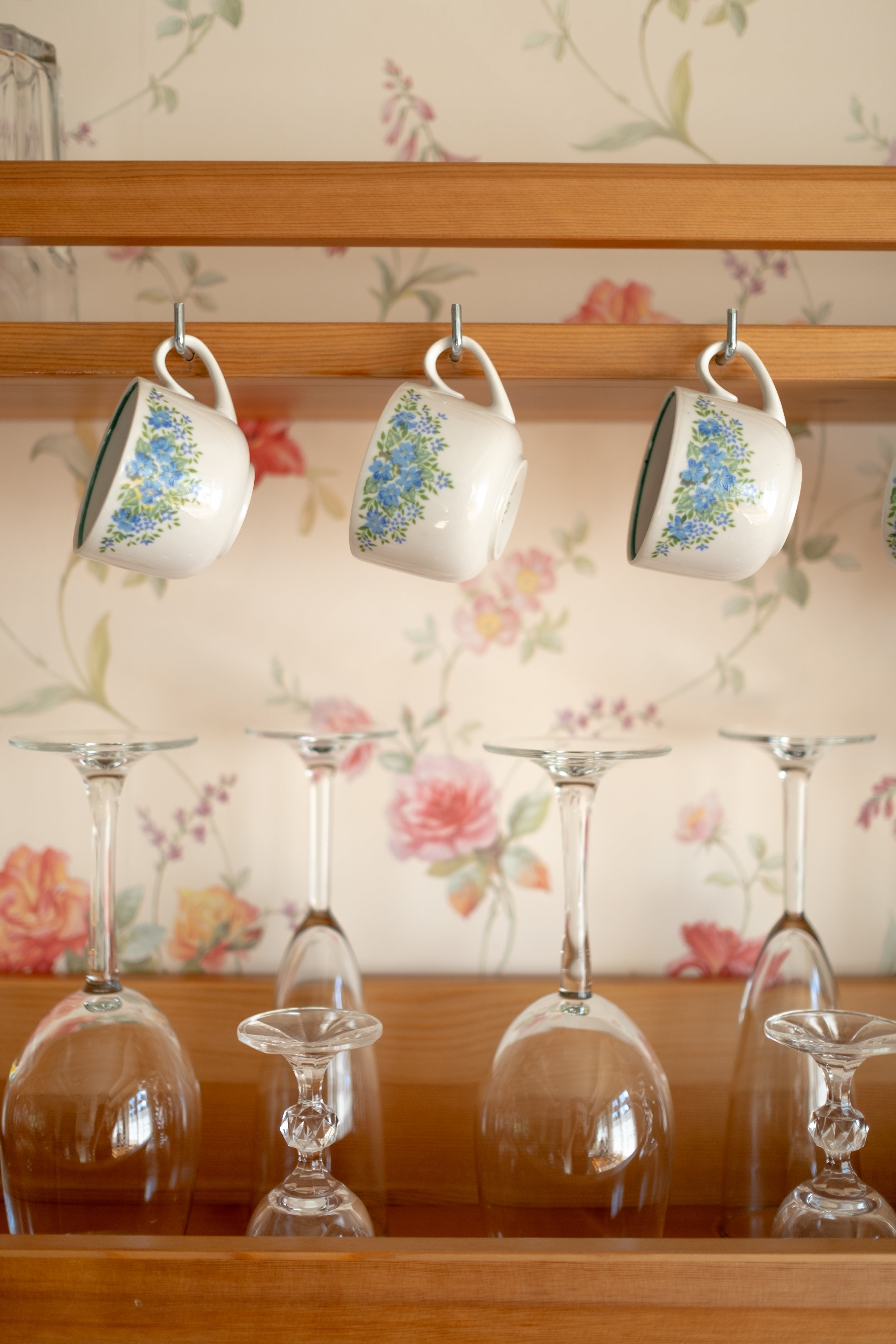 An old fashioned kitchen with flower wallpaper and glasses.